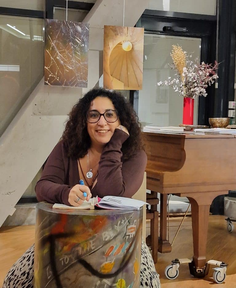 Aramenne, médium, souriante, assise à une table avec un carnet